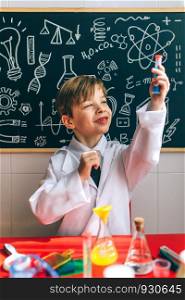 Boy dressed as chemist looking test tube playing with chemistry game in front of a blackboard with drawings