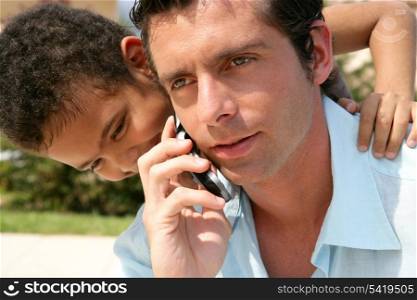 boy embracing his father while he is talking on his cell