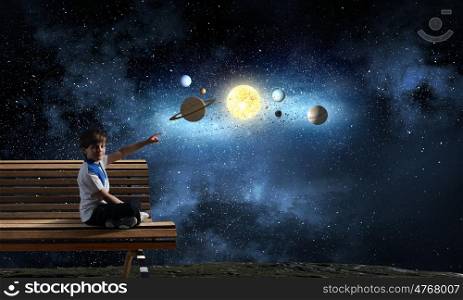 Boy exploring space. Cute school boy sitting on bench and pointing with finger on planets