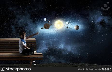 Boy exploring space. Cute school boy sitting on bench and pointing with finger on planets