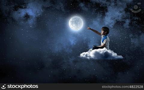 Boy exploring world. Cute school boy sitting on cloud and touching moon with finger