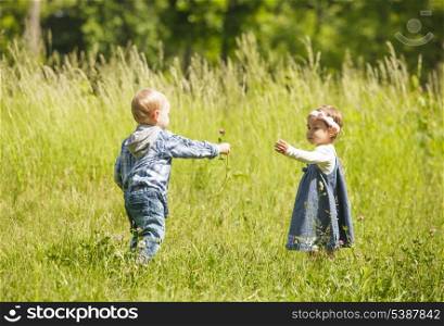 Boy gives a flower to girl. Little kids play outdoors