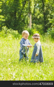 Boy gives a flower to girl. Little kids play outdoors. Boy and girl