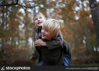 Boy giving friend a piggyback through forest