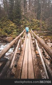 Boy going across wooden bridge over a river during vacation trip in mountains