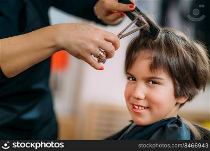 Boy having his hair cut in hairdresser’s salon. Hairdresser for children