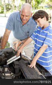 Boy helping his father change the air filter on the car engine.
