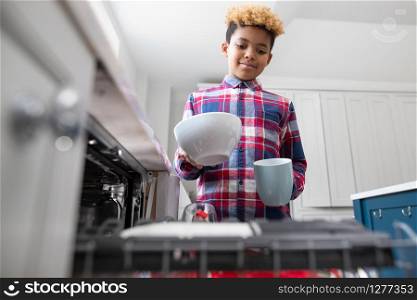 Boy Helping With Chores At Home By Stacking Crockery In Dishwasher