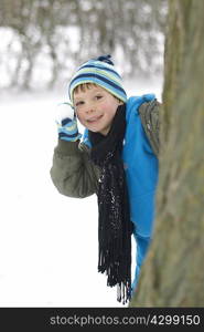 Boy hiding behind tree with snowball