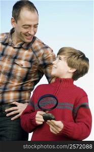 Boy holding a magnifying glass and standing with his father