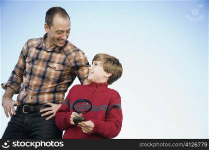 Boy holding a magnifying glass and standing with his father