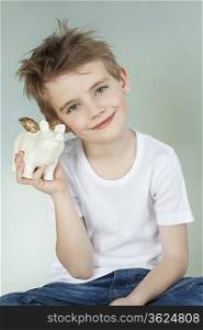 Boy holding a piggy bank over gray background