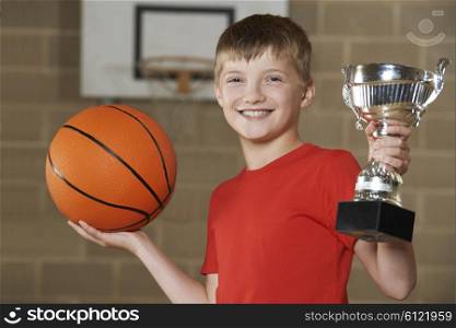 Boy Holding Basketball And Trophy In School Gymnasium