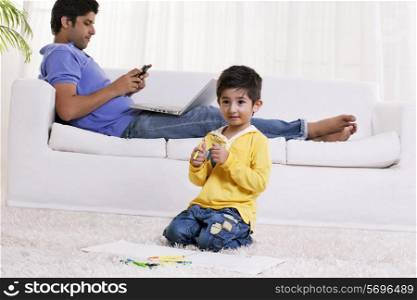 Boy holding felt tip pen with father using cell phone in the background
