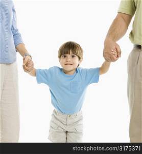 Boy holding hands with parents standing against white background.