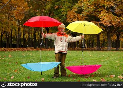 Boy in autumn park. Has control over four multi-coloured umbrellas.