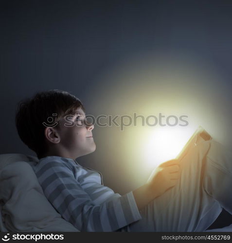 Boy in bed. Cute boy sitting in bed and using tablet pc