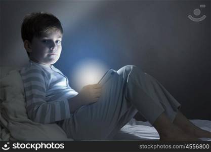 Boy in bed. Cute boy sitting in bed and using tablet pc