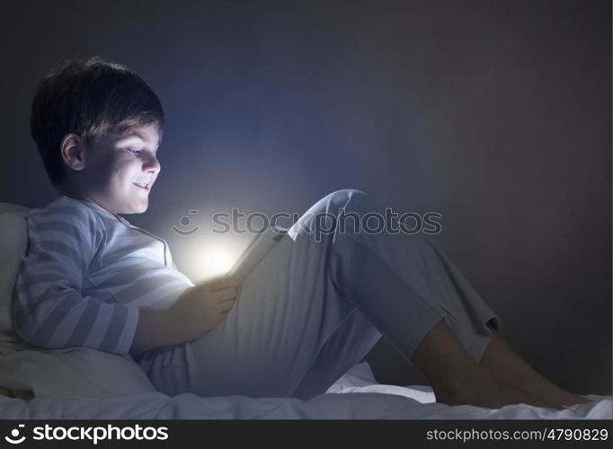 Boy in bed. Cute boy sitting in bed and using tablet pc