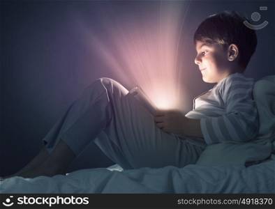 Boy in bed. Cute boy sitting in bed and using tablet pc