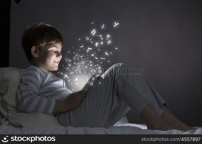 Boy in bed. Cute little boy sitting in bed and using tablet pc