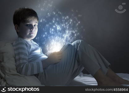 Boy in bed. Cute little boy sitting in bed and using tablet pc