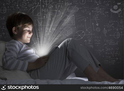 Boy in bed. Cute little boy sitting in bed and using tablet pc