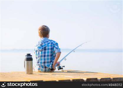 Boy in blue shirt sit on a pie. Boy in blue shirt sit on a pier with a fishing rod by the sea