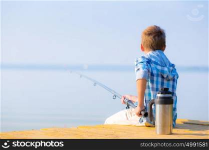Boy in blue shirt sit on a pie. Boy in blue shirt sit on a pier with a fishing rod by the sea