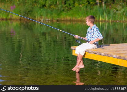 Boy in blue shirt sit on a pier with a fishing rod by the sea