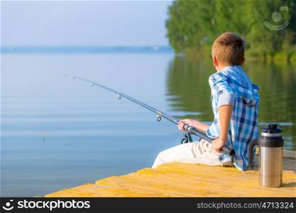 Boy in blue shirt sit on a pier with a fishing rod by the sea