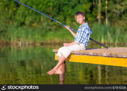 Boy in blue shirt sit on a pier with a fishing rod by the sea