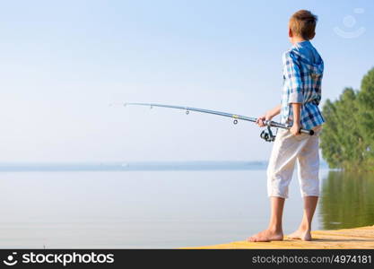 Boy in blue shirt standing on a pie. Boy in blue shirt standing on a pier with a fishing rod by the sea