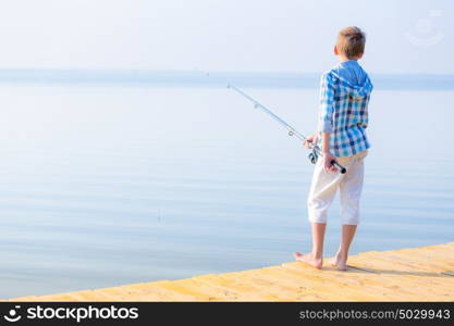 Boy in blue shirt standing on a pie. Boy in blue shirt standing on a pier with a fishing rod by the sea