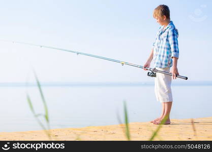 Boy in blue shirt standing on a pie. Boy in blue shirt standing on a pier with a fishing rod by the sea