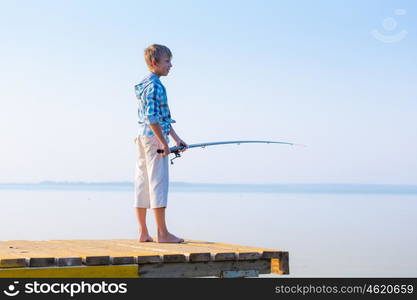 Boy in blue shirt standing on a pier with a fishing rod by the sea