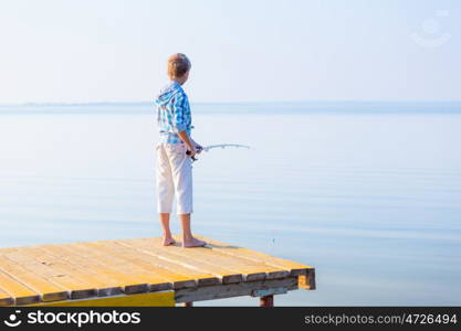 Boy in blue shirt standing on a pier with a fishing rod by the sea