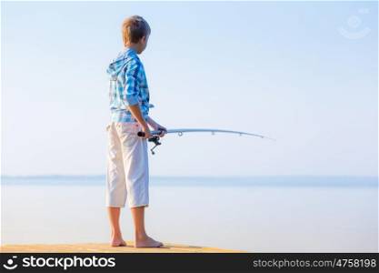 Boy in blue shirt standing on a pier with a fishing rod by the sea