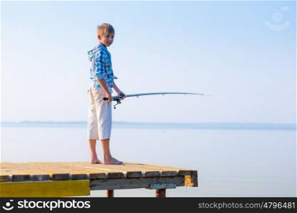 Boy in blue shirt standing on a pier with a fishing rod by the sea