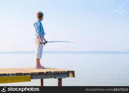 Boy in blue shirt standing on a pier with a fishing rod by the sea