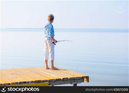 Boy in blue shirt standing on a pier with a fishing rod by the sea. Boy in blue shirt standing on a pie