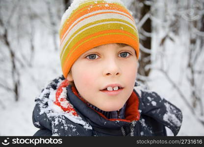 boy in cap with snow on shoulders in wood in winter