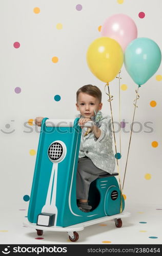 Boy in costume designer on a toy bike with balloons on a white background. boy on a toy motorcycle on a white background