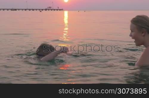Boy in goggles learning to swim with his mother against of beautiful sunset