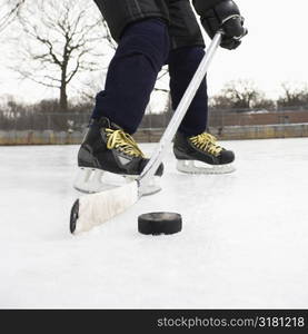 Boy in ice hockey uniform skating on ice rink moving puck.