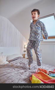 Boy in pyjamas jumping on bed in loft room