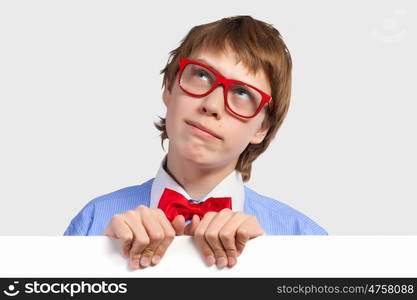 Boy in red glasses holding white square. Image of young boy smiling thoughtfully holding white square. Place for advertisement