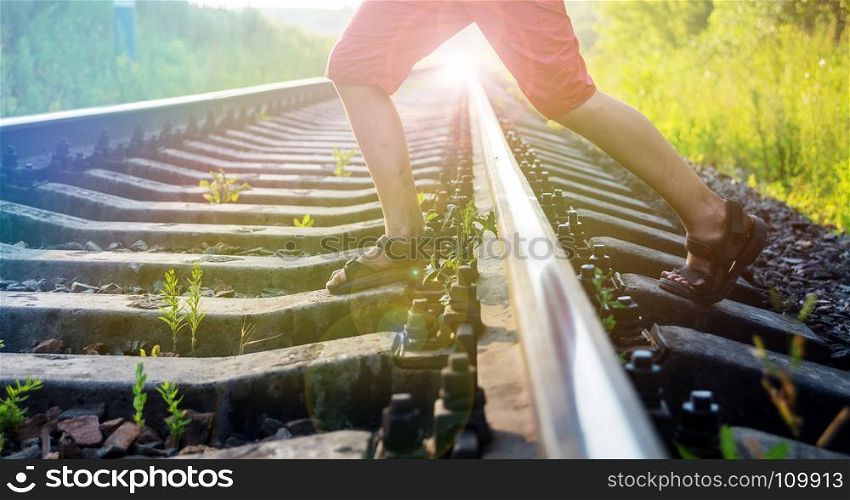 Boy in red shorts with stained feet steps over the rails of the railway, being exposed to danger