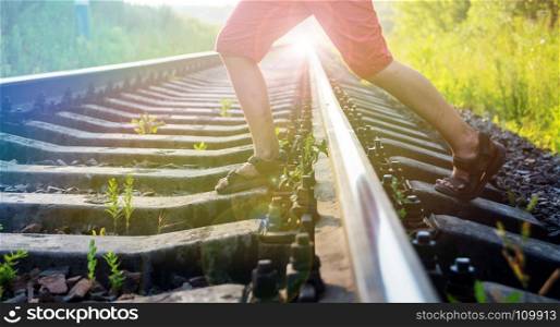 Boy in red shorts with stained feet steps over the rails of the railway, being exposed to danger