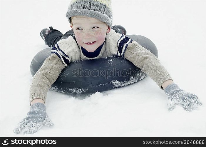 Boy in winter clothing sledging on an inner tyre